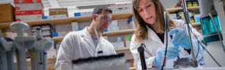Two people in a scientific lab, one observing the other pipetting